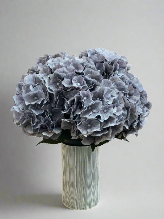A high quality artificial grey Hydrangea flower arrangement displayed in a modern off white ceramic vase with charcoal pinstripe.