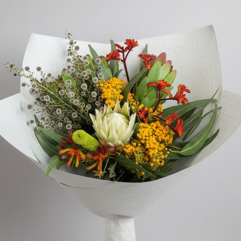 A bouquet of vibrant native flowers including shades of yellow, red, and green, arranged beautifully in a large glass vase.