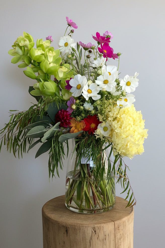 Vase of colorful flowers on a wooden stand against a plain background