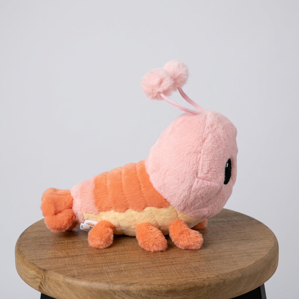 A pink caterpillar plush toy with orange and yellow stripes, sitting on a round wooden stool in front of a white cabinet.