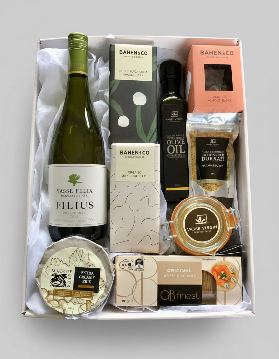 A hamper box containing a variety of gourmet food items including a bottle of wine, duck pate', olive oil, dukkah, crackers, cheese, quince paste, and chocolate.