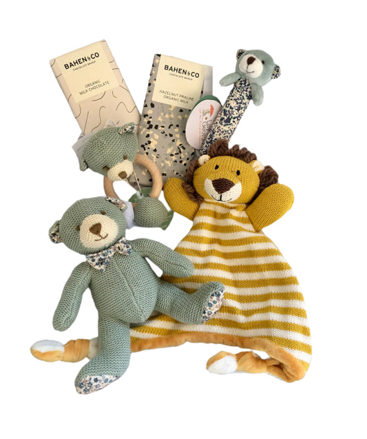 A collection of baby gift items including a knitted mini bear, a stick rattle, a bear teether, a lion comforter, and two chocolate bars.