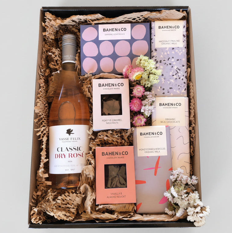 Gift box with a bottle of wine, snacks, and decorative items on a light gray background