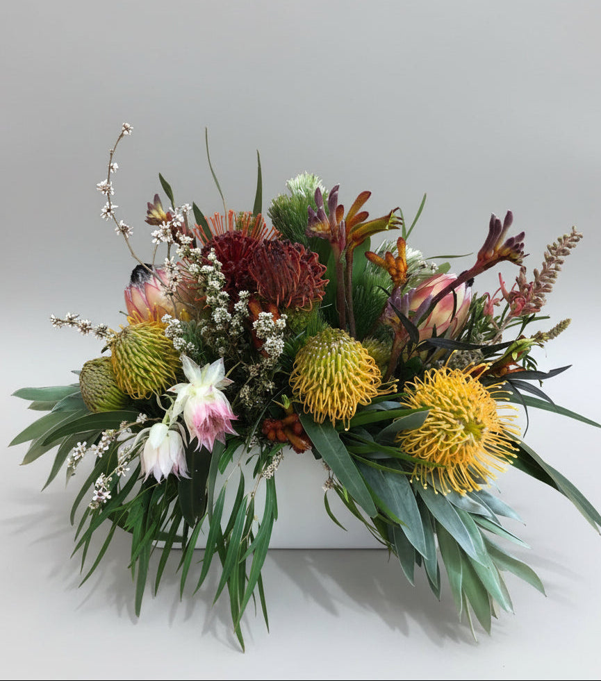 A table arrangement of various native flowers and foliage in a white ceramic rectangular vase.