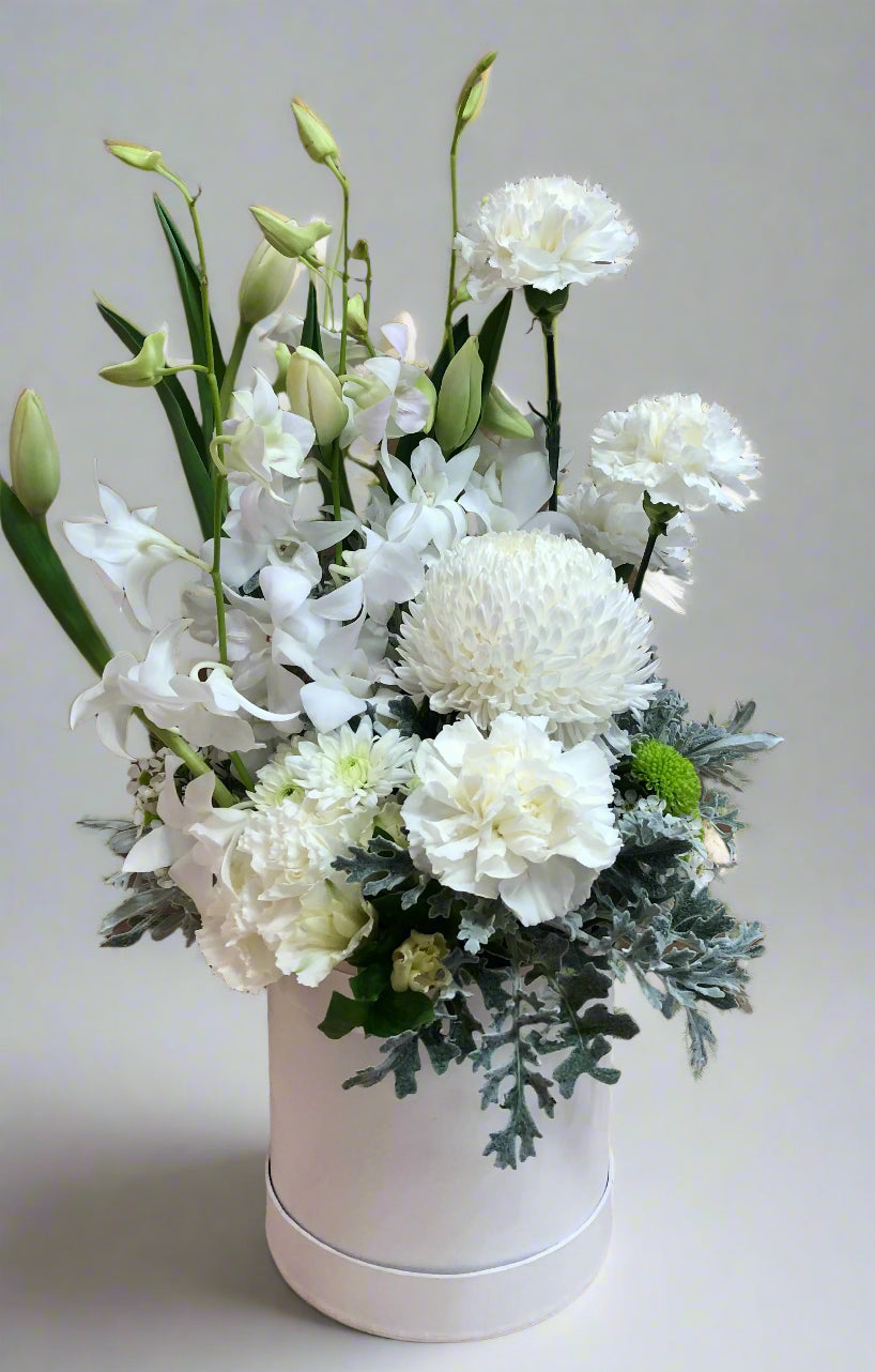 A medium-sized arranged bouquet containing white and green flowers, presented in a white container.
