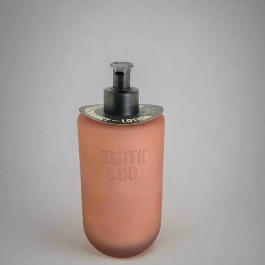 Pink soap dispenser with black pump on a black surface against a white background