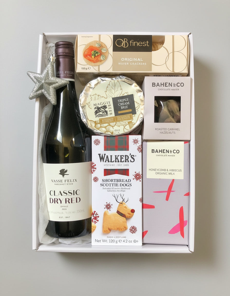 Gift box with a bottle of wine, cheese, and other snacks on a dark surface