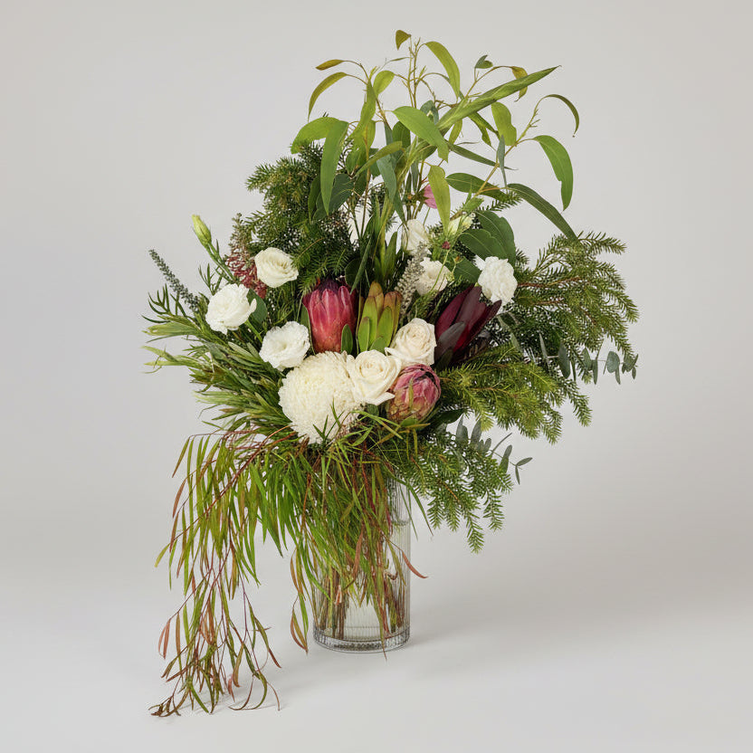 Bouquet of flowers with greenery in a clear vase on a light gray background