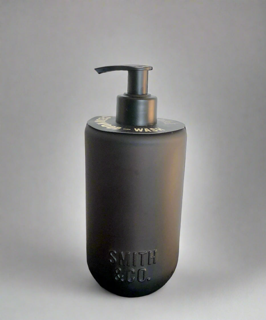 Black soap dispenser with pump on a black surface against a white background