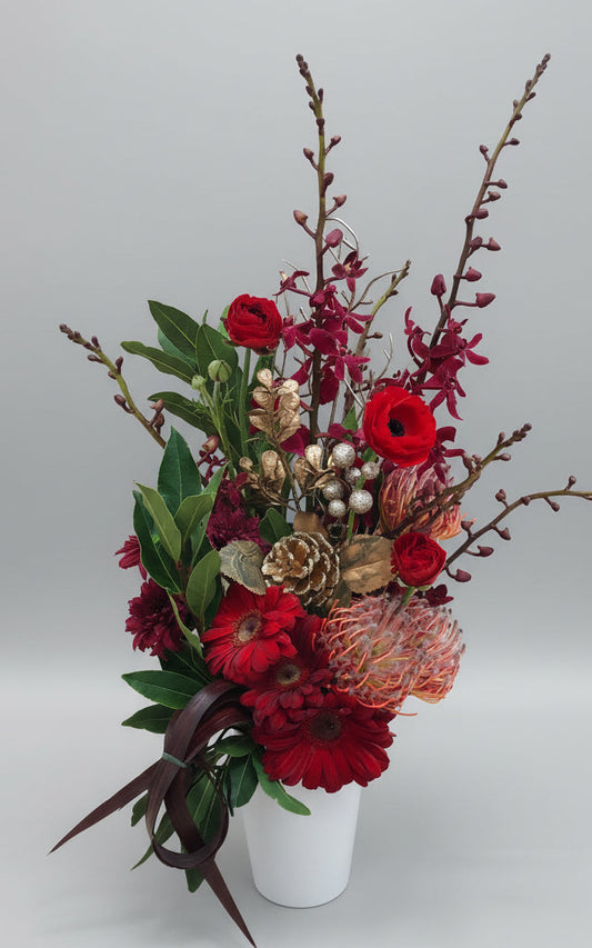 A decorative Christmas flower vase arrangement with a white ceramic vase, filled with a variety of flowers including red and green plants, and adorned with Christmas bling.