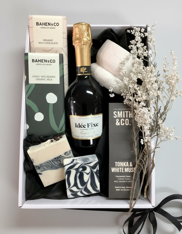 Gift box with champagne, chocolate, and flowers on a light gray background