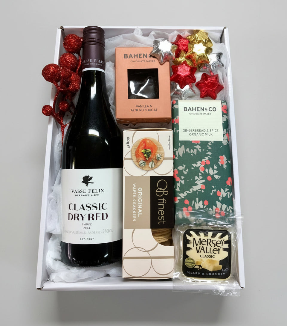 Gift box with a bottle of Vase Felix Classic Dry Red wine, a bar of chocolate, and a small bottle of Merlot Valley Classic on a wooden surface.