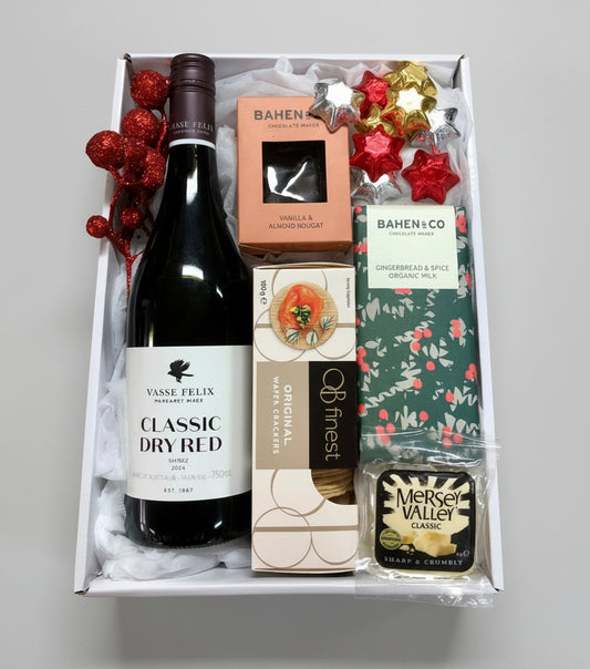 Gift box with a bottle of Vase Felix Classic Dry Red wine, a bar of chocolate, and a small bottle of Merlot Valley Classic on a wooden surface.