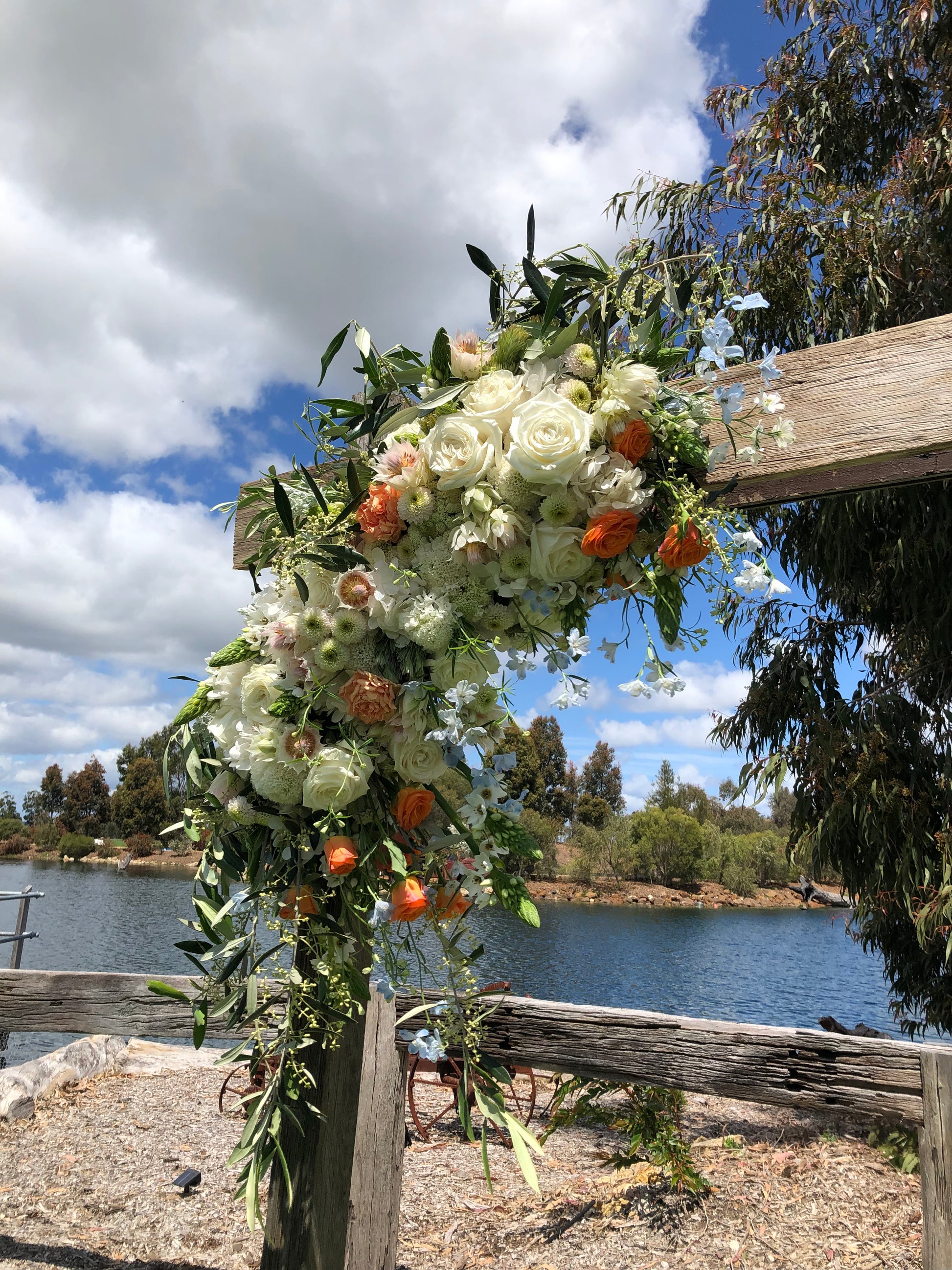 Floral arrangement with white and orange flowers by a body of water.