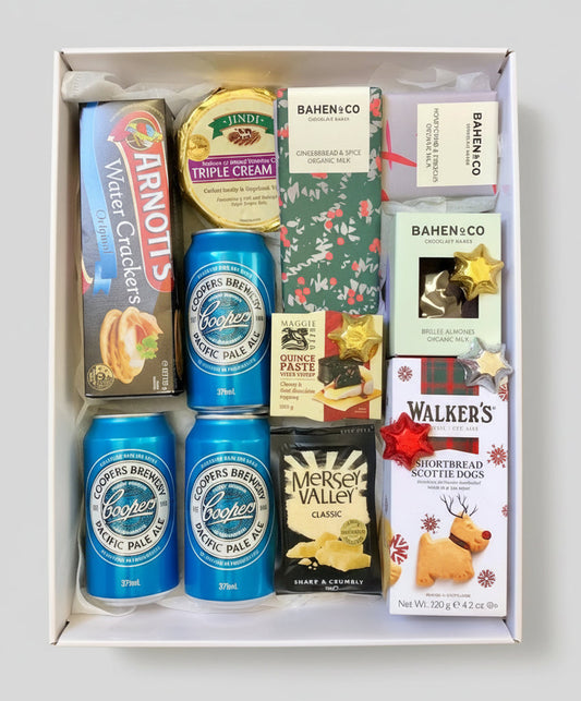 Gift box with beer cans, snacks, and treats on a wooden surface