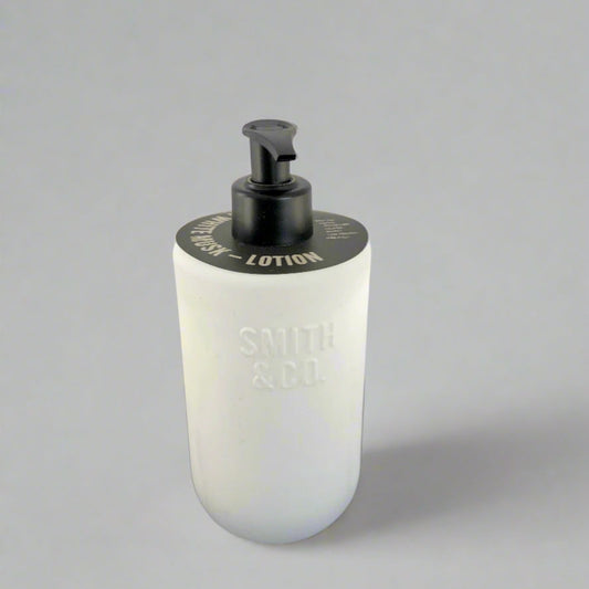 White lotion bottle with black pump on a black surface and white background