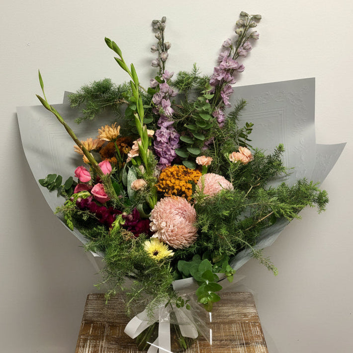 Bouquet of flowers wrapped in paper on a wooden stand against a plain background